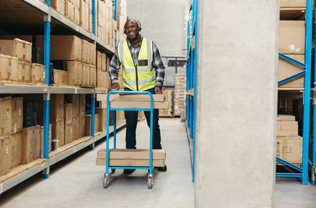 Happy logistics pushing a trolley while picking orders in a warehouse
