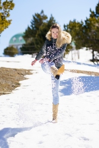 Blonde happy woman kicking snow in a snow covered forest in the mountains