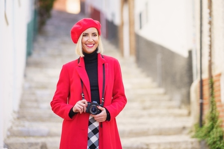 Cheerful female traveler with camera smiling on narrow street during vacation