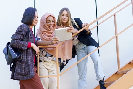 Smiling young diverse women using tablet on stairs
