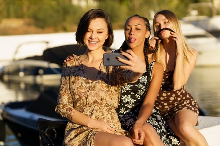 Funny diverse women taking selfie on smartphone on seafront