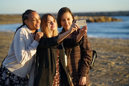 Content diverse women taking selfie on coast