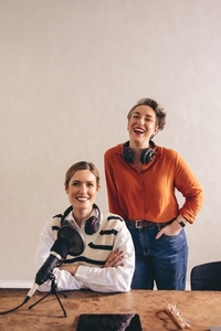 Two female podcasters smiling at the camera in a studio