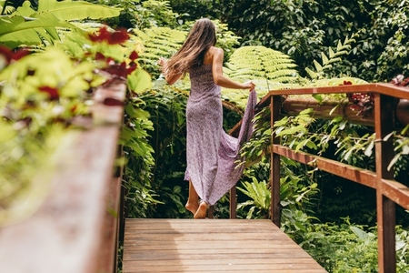 Woman in beautiful dress walking on wooden bridge in nature