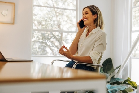 Cheerful businesswoman talking on the phone in her home office