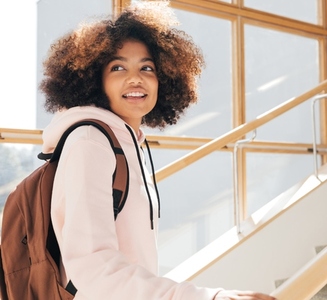Happy girl with curly hair looking back while going up on school stairs