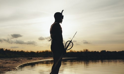 Male diver going spearfishing at sunset