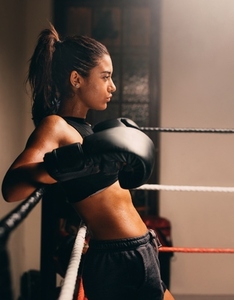 Muscular female boxer leaning against the ropes in a boxing ring
