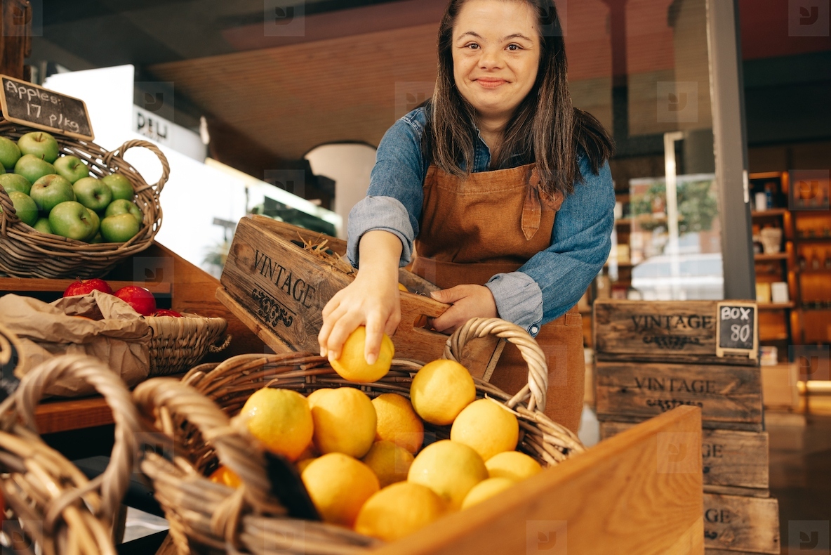 Cheerful woman with Down syndrome restocking fresh fruits in a store