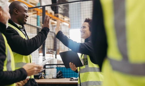 Successful warehouse workers high fiving each other during a meeting