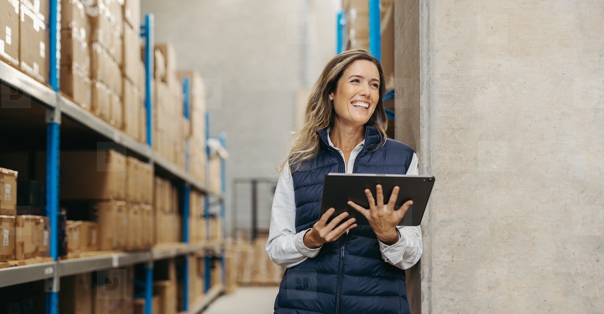 Happy young woman holding a digital tablet in a warehouse