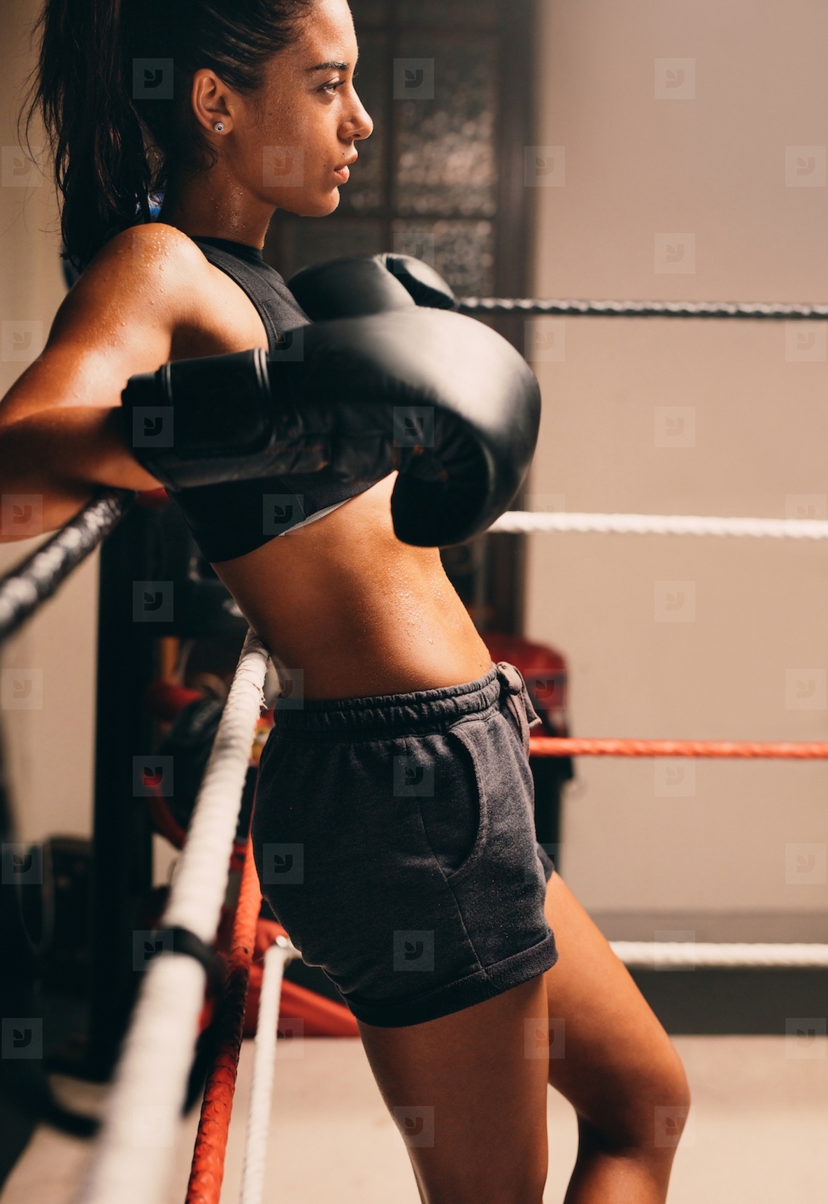 Confident female boxer leaning against boxing ring ropes