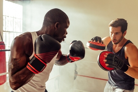 Athletic young man training with his boxing coach in a gym