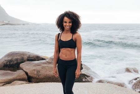 Smiling woman in fitness wear posing against the ocean after training