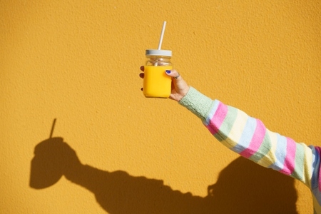 Female hands holding a glass tumbler with lid and straw  to take away  filled with fresh orange juice
