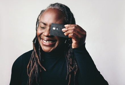 Cheerful woman with dreadlocks smiling while holding a credit card