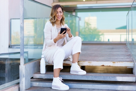 Middle aged woman using smartphone sitting on steps near her office  Famela taken a coffee break