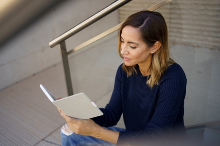 Middle aged woman reading with her e book on a coffee break near her office