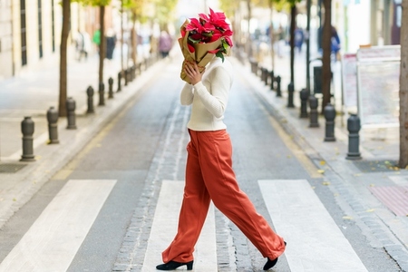 Woman covering face with red flowers while crossing street
