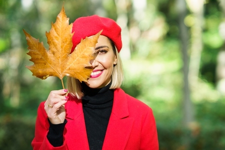 Smiling woman covering face with maple leaf