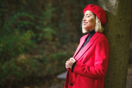 Gentle female wearing red beret and jacket standing near tree