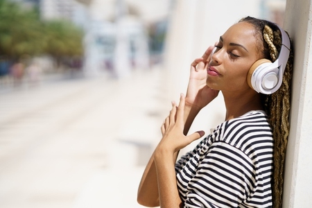 Young black female listening to music with wireless headphones outdoors
