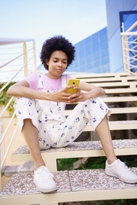Black woman texting with her smartphone  sitting on steps of a modern building