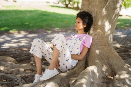 Pensive black woman sitting near tree