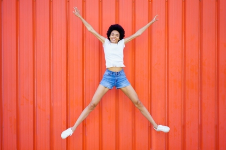 Joyful black woman jumping near wall