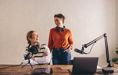 Happy female podcasters smiling at each other in a home studio