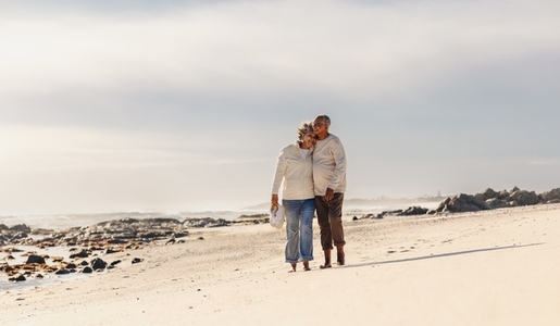 Romantic elderly couple walking barefoot on beach sand