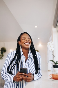 Cheerful black businesswoman laughing happily while holding a smartphone in a cafe