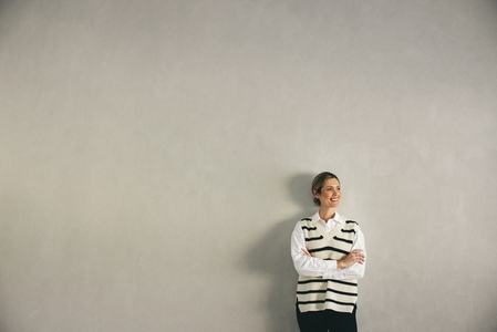 Smiling businesswoman looking away while standing against a wall