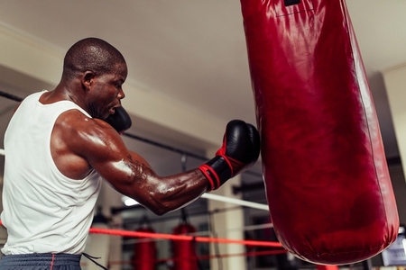 Determined African boxer landing a punch on a red leather bag