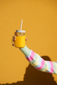 Female hand holding a glass tumbler with lid and straw  to take away  filled with fresh orange juice