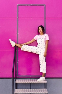 Asian woman looking at camera with serious expression  raising one leg over railing near pink wall