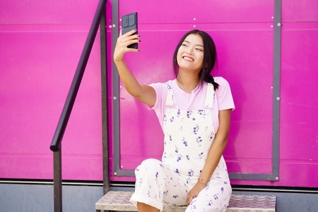 Young Chinese woman taking a photo or video selfie with her smartphone  to post on social media