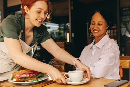Happy young waitress serving a customer in a modern cafe