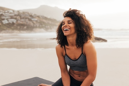 Laughing female with closed eyes sitting on a beach relaxing after an outdoor workout