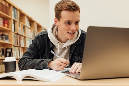 Smiling guy looking at laptop screen while sitting in library