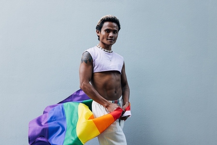 Young guy with LGBT flag posing at grey wall outdoors