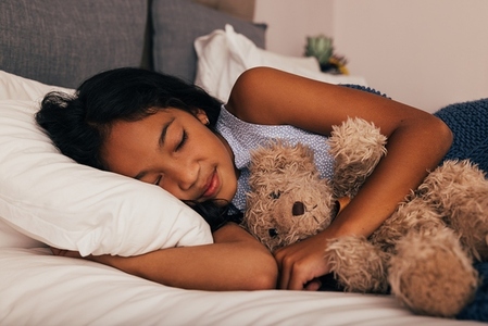 Girl sleeping on a bed holding a teddy bear