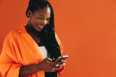 Smiling black woman sending a text message on her smartphone in a studio