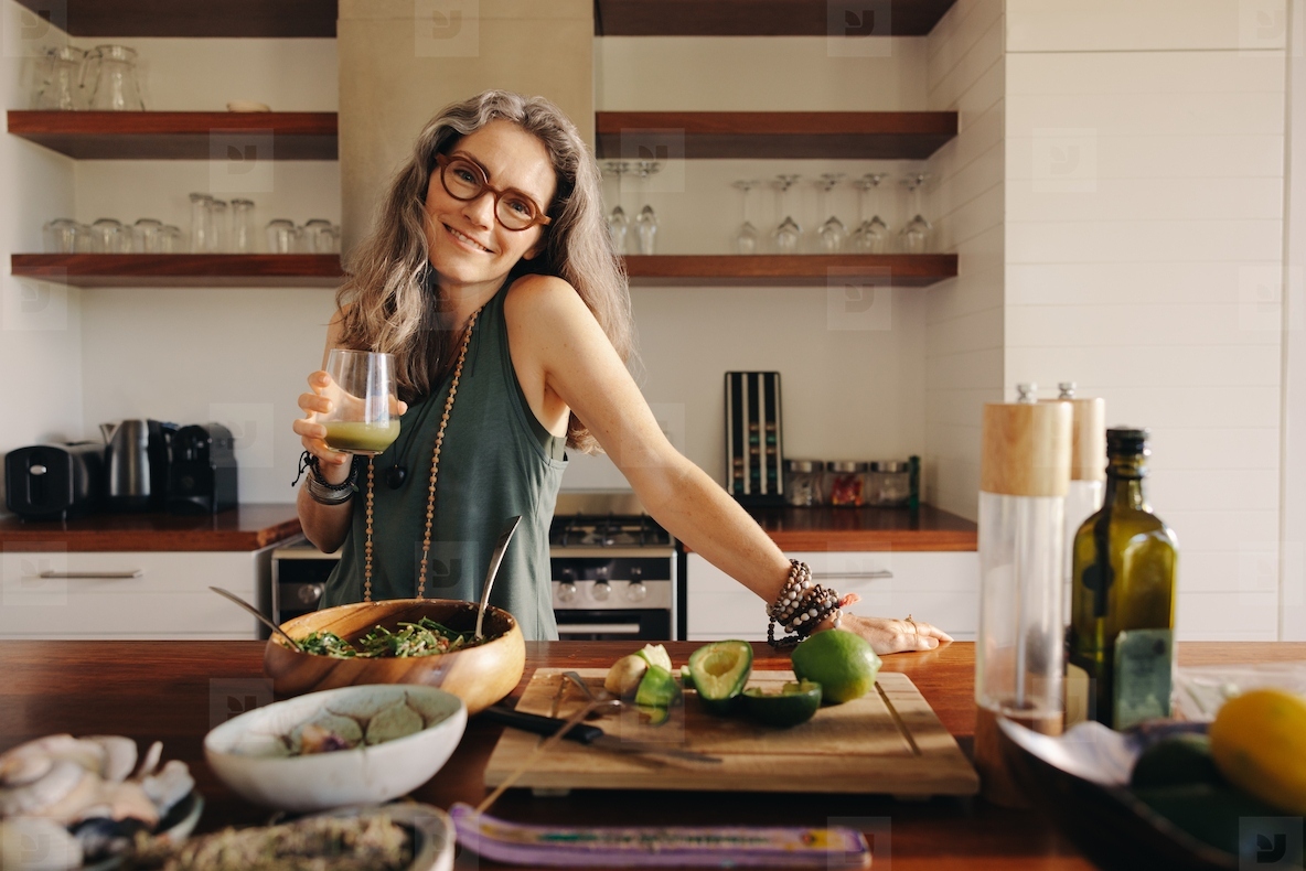 Vegetarian woman holding a glass of green juice in her kitchen