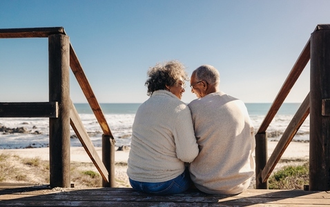 Happy elderly couple sitting on a wooden foot bridge at the beach