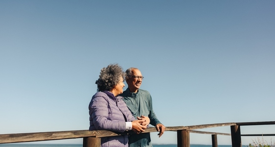 Happy elderly couple standing on a wooden seaside bridge