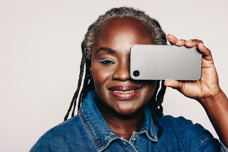 Mature woman holding a smartphone over her eye