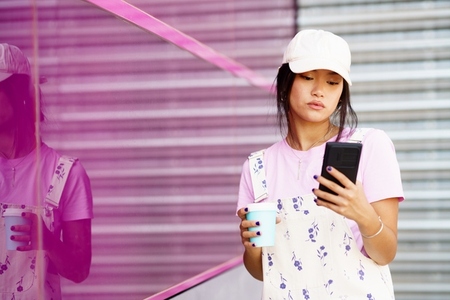 Asian woman using smartphone near pink glass wall