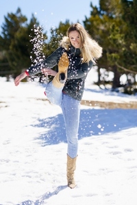 Young happy woman kicking snow in a snow covered forest in the mountains