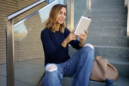 Glad woman enjoying reading on steps